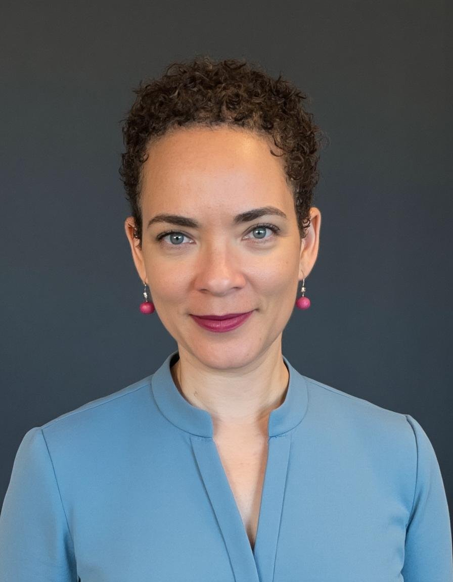 Professional headshot of Dr. Aynen Vallis wearing a blue top against a dark background for her practice.